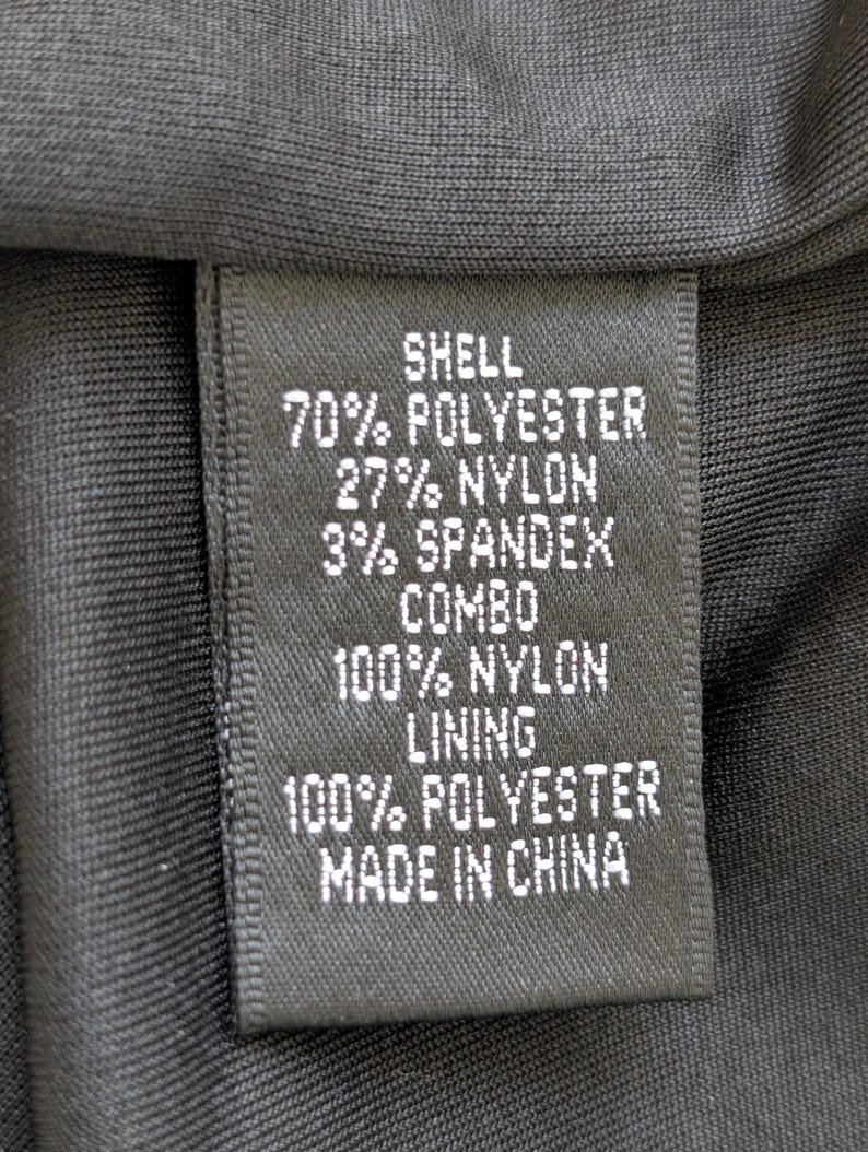 May include: A black fabric tag with white text detailing the material composition of a garment. The tag lists "SHELL" with 70% polyester, 27% nylon, and 3% spandex. It also includes "COMBO" and "LINING" details, and states "MADE IN CHINA."