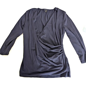 May include: A navy blue long-sleeve top with a draped, asymmetrical design. The top features a V-neckline and ruching on the side, creating a flattering silhouette. The fabric appears soft and comfortable, suitable for various occasions.