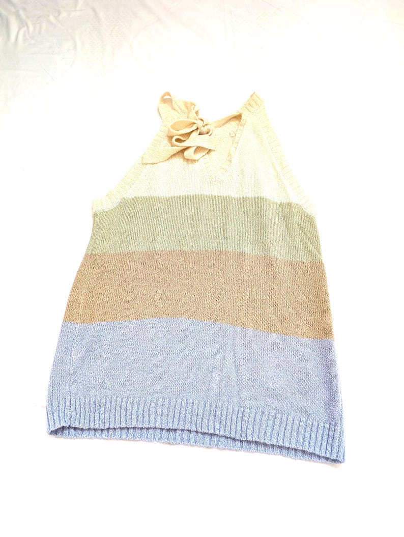May include: A striped halter top with a cream-coloured bow at the neckline. The top has horizontal stripes in cream, green, tan, and light blue. The bottom hem is a ribbed knit. The garment is sleeveless.