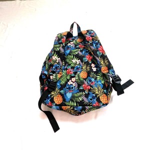 May include: Black backpack with a colorful tropical pattern featuring blue cartoon characters, pineapples, and flowers. The backpack has black straps and a top handle.