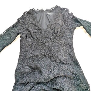 May include: Black lace dress with long sleeves and a V-neckline. The dress features a floral lace pattern and a ruffled hem. The dress has a fitted bodice and a flared skirt. The dress is made of a delicate lace fabric.