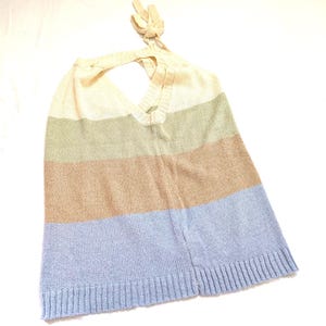 May include: A knitted halter top with a colour block design. The top features horizontal stripes in cream, olive green, tan, and light blue. The halter straps are tied at the back of the neck.