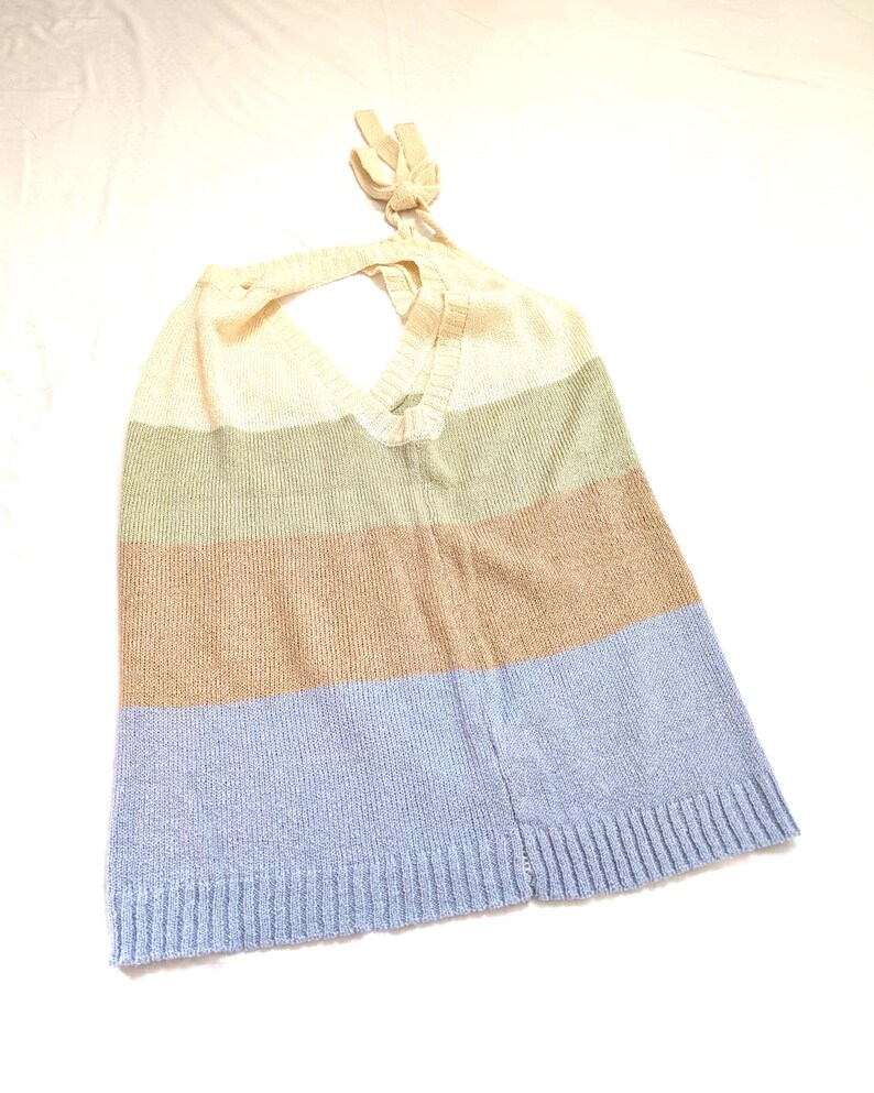 May include: A knitted halter top with a colour block design. The top features horizontal stripes in cream, olive green, tan, and light blue. The halter straps are tied at the back of the neck.