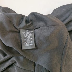 May include: Close-up of a black garment with a fabric content label. The label reads: 70% Polyester, 27% Nylon, 3% Spandex, Combo 100% Nylon, Lining 100% Polyester, Made in China. The garment is likely a dress or top.