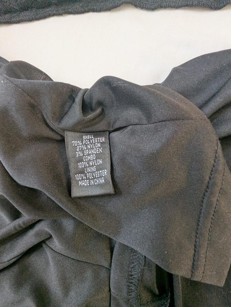 May include: Close-up of a black garment with a fabric content label. The label reads: 70% Polyester, 27% Nylon, 3% Spandex, Combo 100% Nylon, Lining 100% Polyester, Made in China. The garment is likely a dress or top.