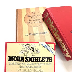May include: Three books: a tan and white striped "Webster's New Students Dictionary", a red "College Dictionary", and a rectangular card titled "MORE SNIGLETS". The card features a cartoon and text: "(snig'lit): any word that doesn't appear in the dictionary, but should".