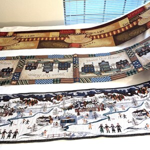 May include: Three decorative fabric table runners. The top runner features coffee cups and the words "Java", "Espresso", and "Cafe". The middle runner has houses and the text "Bless Our Home". The bottom runner depicts a winter scene.
