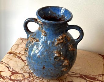 May include: A blue ceramic vase with two handles and a textured surface. The vase has a round body and a wide opening. The vase is decorated with raised, brown-colored accents.