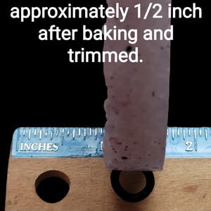 K&ouml;nnte beinhalten: Nahaufnahme eines hellfarbigen, strukturierten Objekts mit dunklen Flecken, gemessen mit einem Lineal. Der Text gibt an, dass die Dicke nach dem Backen und Trimmen etwa 1,27 cm betr&auml;gt. Unten befindet sich ein schwarzer Ring.