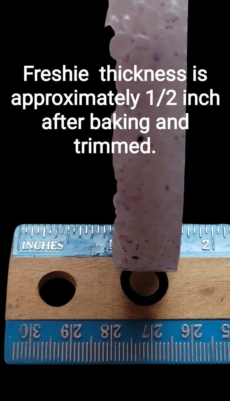 K&ouml;nnte beinhalten: Nahaufnahme eines hellfarbigen, strukturierten Objekts mit dunklen Flecken, gemessen mit einem Lineal. Der Text gibt an, dass die Dicke nach dem Backen und Trimmen etwa 1,27 cm betr&auml;gt. Unten befindet sich ein schwarzer Ring.