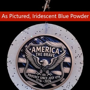 May include: A circular ornament featuring a central emblem with a bald eagle, the text AMERICA THE BRAVE, and PROUDLY SINCE JULY 4TH 1776-2026. The emblem is set within a translucent, glitter-flecked border. A red banner reads As Pictured, Iridescent Blue Powder.