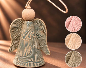 Puede incluir: Un adorno de ángel de cerámica con esmalte verde salvia brillante y patrones florales en relieve. Presenta una cabeza redonda de color terracota sin esmaltar y un lazo de cuerda beige para colgar. Tres recuadros circulares muestran el mismo diseño en rosa, beige y oliva.