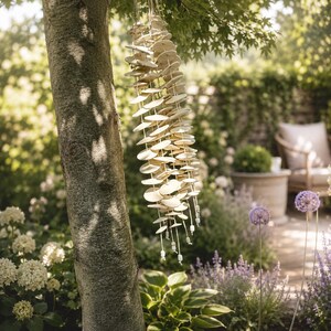 May include: A hanging wind chime composed of numerous small, circular, off-white ceramic discs strung together on vertical cords. The discs are arranged in multiple parallel strands, each ending with a small, cylindrical bead at the bottom.