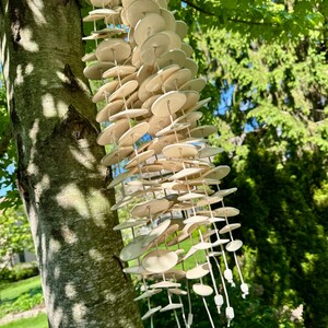 May include: A hanging wind chime composed of numerous off-white, circular ceramic discs strung together on multiple vertical cords. The discs are arranged in several cascading strands, each finished with a small, square ceramic bead at the bottom.