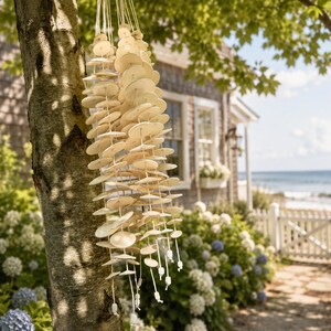 May include: A hanging wind chime composed of numerous small, circular, off-white ceramic discs strung together on thin white cords. The discs are arranged in multiple vertical strands that hang from a central point, creating a layered, textured appearance.