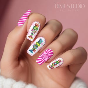 May include: A hand with manicured nails featuring a festive design. The nails showcase a mix of white and pink, with candy cane stripes and whimsical nutcracker illustrations. The text "DIME STUDIO NAIL COUTURE" is visible.