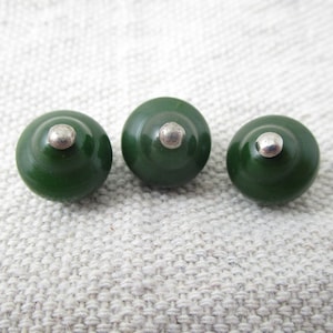 May include: Three green and silver round buttons with a raised center. The buttons are arranged in a row.