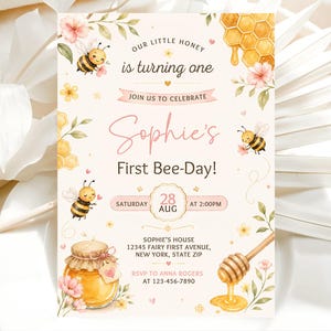 May include: A whimsical invitation with a bee theme. The design features a honey pot, honeycomb, and cartoon bees. The text reads "Our Little Honey is turning one" and "Sophie's First Bee-Day!" with event details.