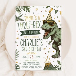 Pu&ograve; includere: Un invito di compleanno rettangolare con un T-Rex verde che indossa occhiali da sole e un cappellino da festa. Il testo recita: THERE'S A THREE-REX ON THE LOOSE! JOIN US TO CELEBRATE CHARLIE'S 3RD BIRTHDAY. Include dettagli della festa e un vulcano.