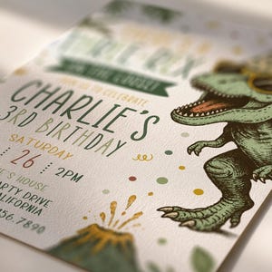 Pu&ograve; includere: Un biglietto d'invito per compleanno con un T-Rex verde che indossa un cappellino da festa e occhiali da sole. Il testo recita: Charlie's 3rd Birthday, Saturday Aug 26, 2pm, Charlie's House, Dino Party Drive, San Diego, California, 123.456.7890. Con vulcano.