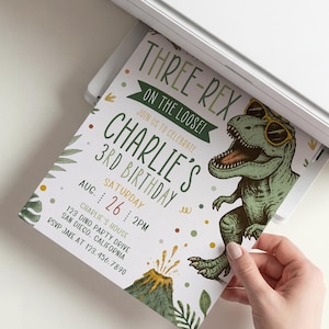 Pu&ograve; includere: Un biglietto d'invito di compleanno stampato con un T-Rex verde che indossa occhiali da sole gialli, un vulcano e foglie tropicali. Il testo recita: THREE-REX ON THE LOOSE! JOIN US TO CELEBRATE CHARLIE'S 3RD BIRTHDAY, SATURDAY AUG 26 2PM, CHARLIE'S HOUSE, 123 DINO PARTY DRIVE.