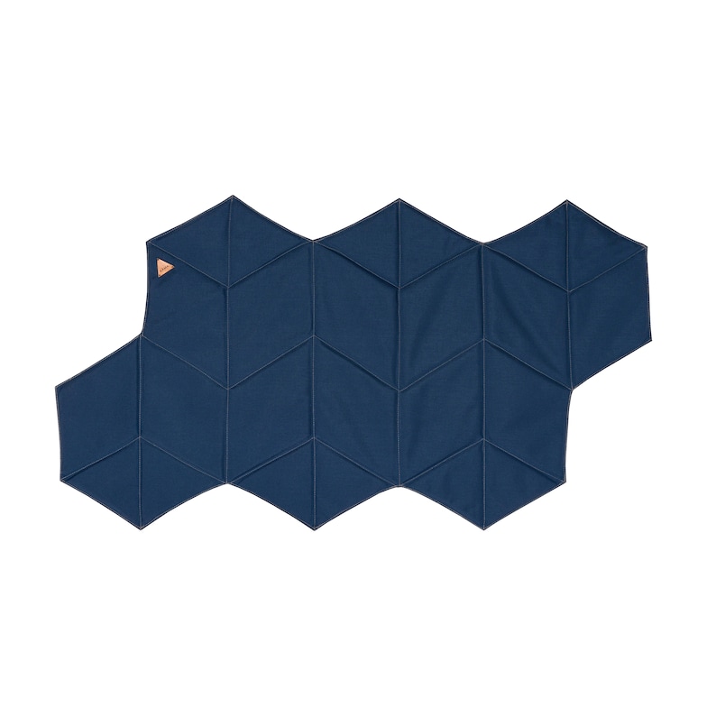 Pu&ograve; includere: Un tappetino blu navy a motivi geometrici con un design a nido d'ape. Il tappetino &egrave; realizzato in tessuto e presenta una serie di forme esagonali collegate. Una piccola etichetta marrone chiaro &egrave; attaccata all'angolo in alto a sinistra. Il tappetino &egrave; su sfondo bianco.