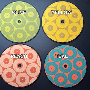 Może przedstawiać: Cztery okrągłe podkładki z wzorem koncentrycznych kół. Podkładki są oznaczone jako "Olive", "Yellow", "Peach" i "Teal".