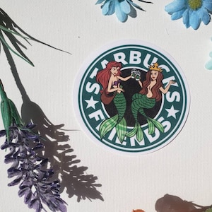 May include: Green and white sticker with the Starbucks logo and the text "Starbucks Friends" in a circle. Two mermaids are holding cups of coffee. One mermaid has red hair and the other has brown hair.