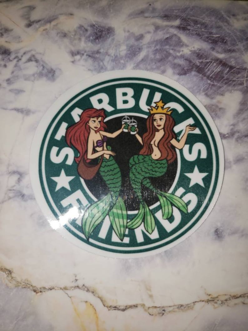 May include: A green and white sticker with the Starbucks logo and the word "Friends" written around it. Two mermaids are holding cups of coffee, one with red hair and one with blonde hair.