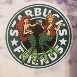 May include: A green and white Starbucks logo with the word "FRIENDS" written around the outside. Two mermaids, one with red hair and one with brown hair, are holding Starbucks cups and smiling.