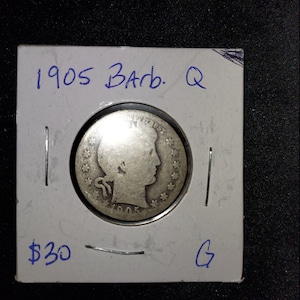 May include: A silver 1905 Barber quarter in a white cardboard holder with the text "1905 Barb. Q" and "$30 G" written in blue ink.