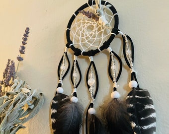 May include: Black and white dreamcatcher with feathers and beads. The dreamcatcher has a white web and black string. The feathers are black with white stripes. The beads are white and clear.
