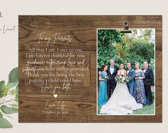 May include: A rustic wooden frame with a photo of a wedding party in a garden setting. The frame has a white inscription that reads "To my Parents, All that I am, I owe to you. I am forever thankful for your guidance, outpouring love and support you have always provided. Thank you for being the best parents a child could have. I love you both. Love Lily, October 30, 2021."