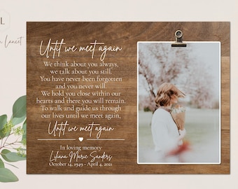 May include: A wooden memorial plaque with a photo of a woman in a white sweater holding flowers. The plaque has a white inscription that reads "Until we meet again" and "In loving memory Liana Marie Sanders October 14, 1949 - April 4, 2021".
