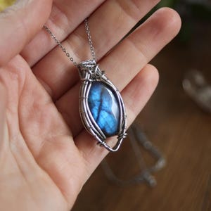 Peut inclure: Un collier pendentif argenté orné d'une pierre de labradorite bleue. La pierre de forme ovale est sertie dans un cadre filaire. Le collier est présenté sur un fond neutre.