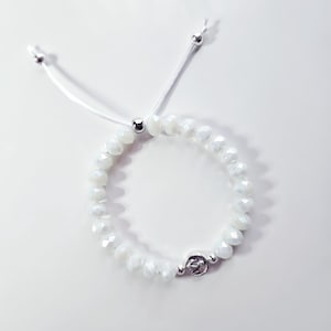 May include: A white beaded bracelet with a silver clasp and adjustable white cord. The bracelet features faceted, iridescent beads and a small silver charm. The cord ends with small silver beads.