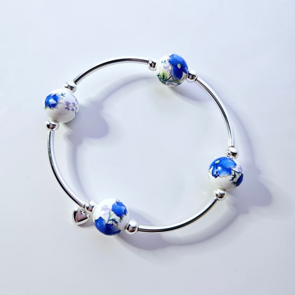 Pulsera "Verdaderamente Bendecido/a", con cuentas de porcelana blanca, diseño floral azul eléctrico pintado a mano y dije de plata.
