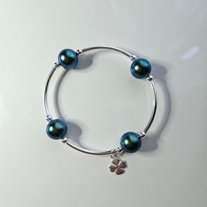 May include: A silver bracelet with four dark green iridescent pearls and a silver four-leaf clover charm.