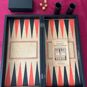 May include: A backgammon board game set featuring a black folding case with a tan interior, red and black triangular points, two black dice cups, four yellow dice, a black storage box, and an instruction booklet titled How to Play Modern Backgammon.
