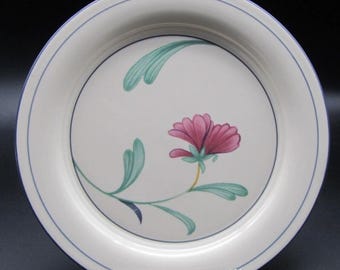 Puede incluir: Un plato de cerámica blanca con un diseño floral. El plato presenta una flor rosa con hojas verdes y un borde azul. El plato es redondo y parece ser parte de un juego de vajilla.