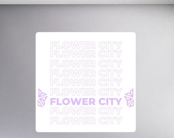 May include: A white sticker with the text "FLOWER CITY" repeated multiple times in a stacked pattern. The text is outlined in white and filled with a light purple color. The text "FLOWER CITY" is larger and in bold in the center of the sticker.