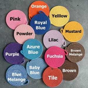 May include: A collection of round, coiled rope coasters in various colors, each labeled with text including Pink, Orange, Yelllow, Royal Blue, Powder, Mustard, Lilac, Purple, Azure Blue, Fuchsia, Brown Melange, Blue Melange, Baby Blue, Tile, and Brown.