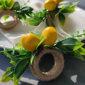 May include: A set of three lemon-themed napkin rings. Each ring is made of natural twine and features a faux lemon and green leaves.