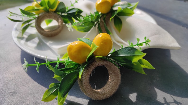 May include: A set of three lemon-themed napkin rings. Each ring is made of natural twine and features a faux lemon and green leaves.
