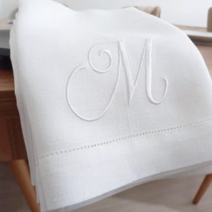May include: White linen hand towel with a single embroidered letter "M" in a script font.