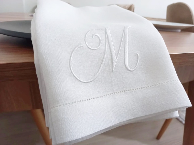 May include: White linen hand towel with a single embroidered letter "M" in a script font.
