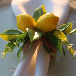 Pu&ograve; includere: Un portatovagliolo decorativo con due limoni gialli e foglie verdi. L'anello &egrave; realizzato in materiale tessuto e tiene un tovagliolo bianco. Piccoli fiori bianchi aggiungono un tocco delicato, perfetto per una tavola estiva.