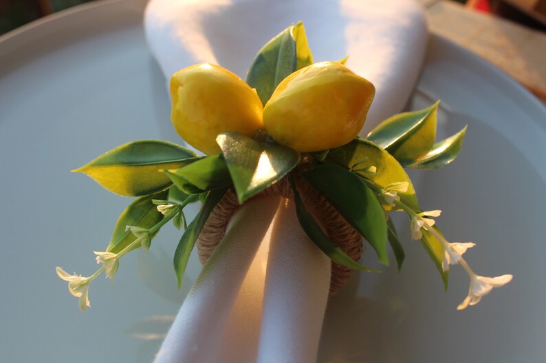 Pu&ograve; includere: Un portatovagliolo decorativo con due limoni gialli e foglie verdi. L'anello &egrave; realizzato in materiale tessuto e tiene un tovagliolo bianco. Piccoli fiori bianchi aggiungono un tocco delicato, perfetto per una tavola estiva.