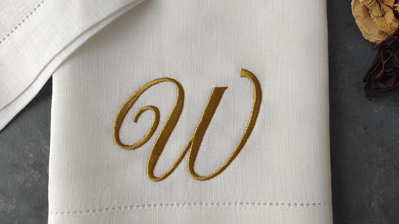 May include: White linen napkin with a gold embroidered letter W.