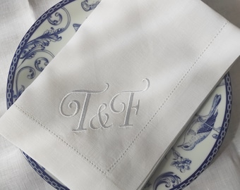 May include: White linen napkin with a gray embroidered monogram "T&F" on a blue and white patterned plate.
